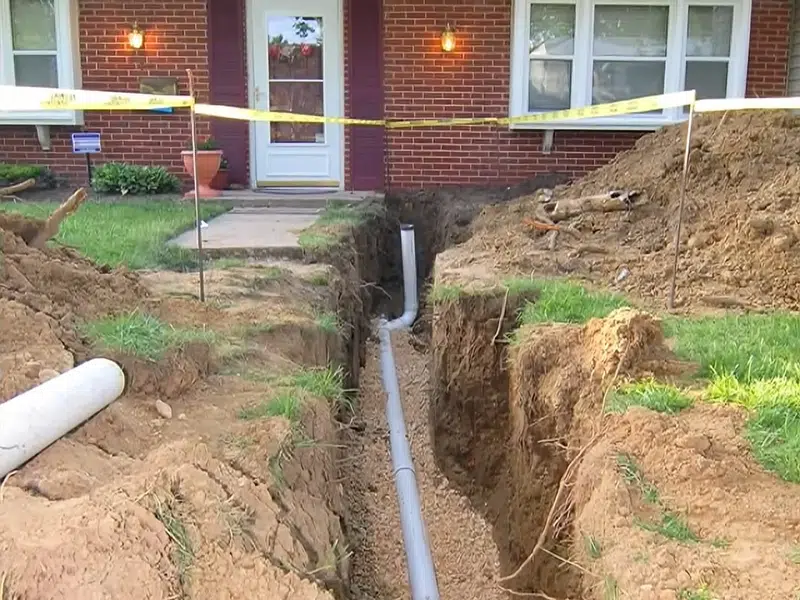 Front yard trench with new sewer pipe near building for sewer line repair in Stanton